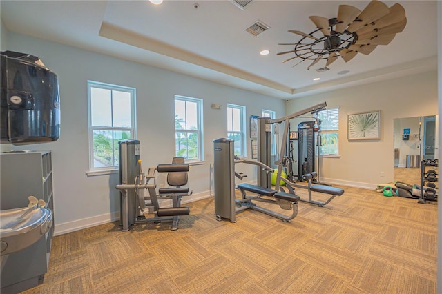 workout room with light colored carpet, a tray ceiling, and ceiling fan