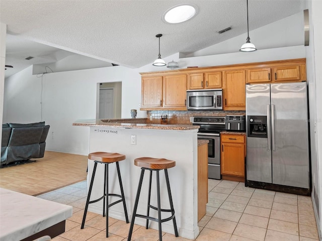 kitchen featuring tasteful backsplash, vaulted ceiling, pendant lighting, appliances with stainless steel finishes, and light tile patterned floors