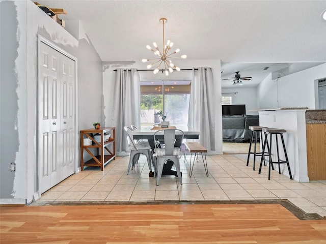 dining area featuring light wood-type flooring, ceiling fan with notable chandelier, and a textured ceiling