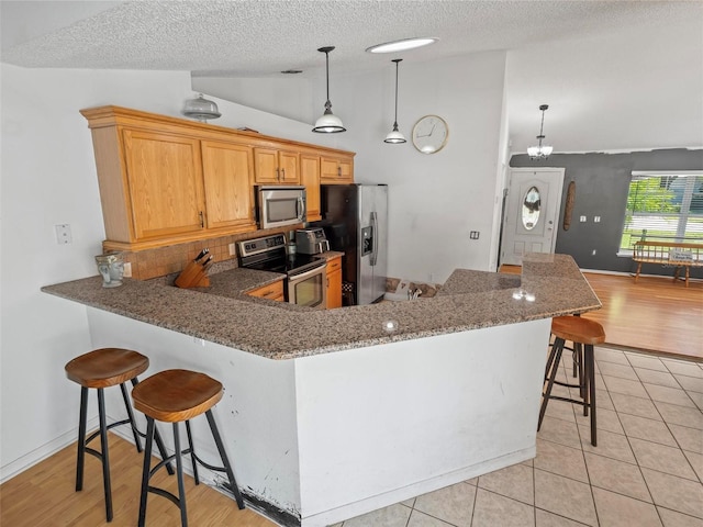 kitchen with decorative light fixtures, vaulted ceiling, kitchen peninsula, a breakfast bar area, and stainless steel appliances