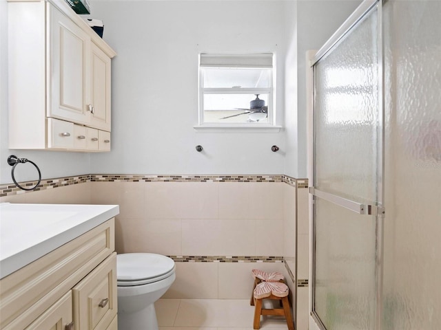 bathroom featuring toilet, a shower with door, tile walls, tile patterned floors, and vanity