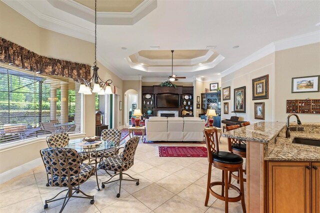 tiled dining room with ceiling fan with notable chandelier, a raised ceiling, crown molding, and sink