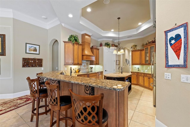 kitchen featuring tasteful backsplash, custom range hood, decorative light fixtures, and a kitchen bar