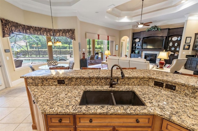 kitchen with light stone counters, hanging light fixtures, a raised ceiling, sink, and ceiling fan