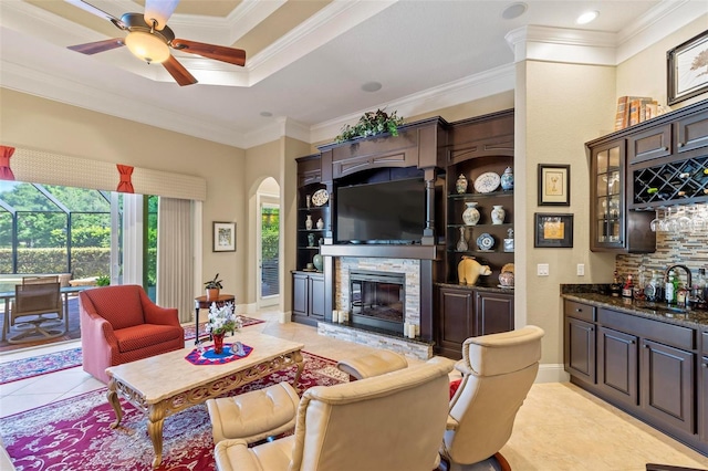 tiled living room featuring a fireplace, sink, ceiling fan, and crown molding