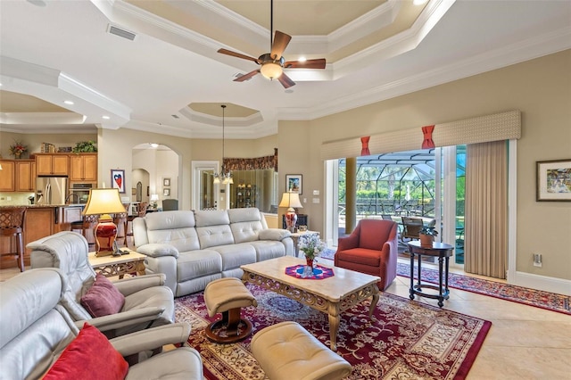 living room with light tile flooring, crown molding, ceiling fan with notable chandelier, and a tray ceiling