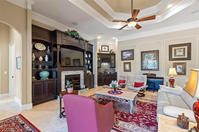 tiled living room featuring ornamental molding, ceiling fan, a raised ceiling, and a fireplace