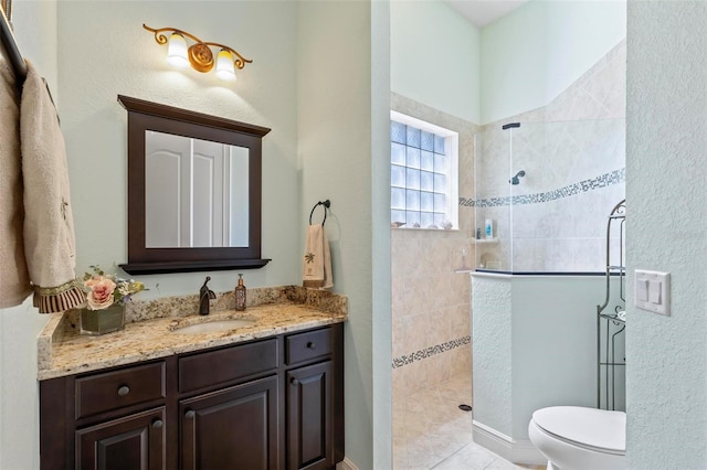 bathroom featuring tile flooring, tiled shower, vanity, and toilet