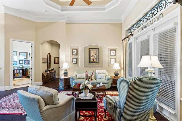 living room with a raised ceiling, crown molding, dark wood-type flooring, and ceiling fan