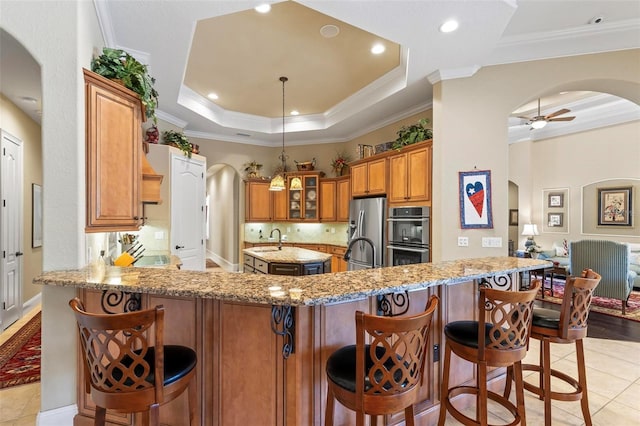 kitchen featuring a kitchen breakfast bar, stainless steel appliances, light stone counters, a tray ceiling, and kitchen peninsula