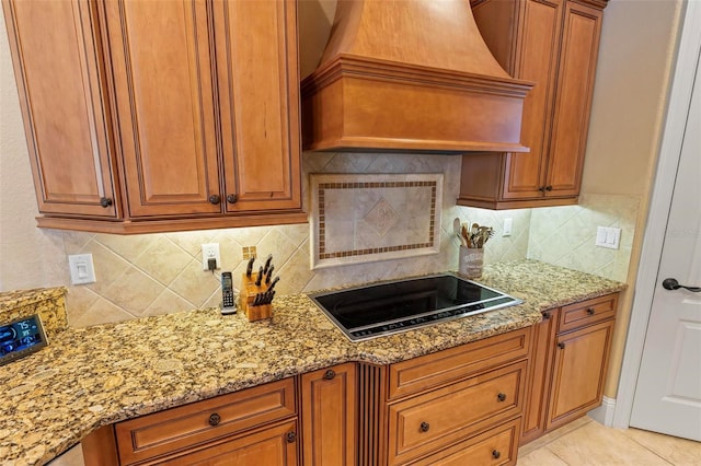 kitchen featuring light stone counters, custom range hood, light tile patterned flooring, black electric cooktop, and decorative backsplash