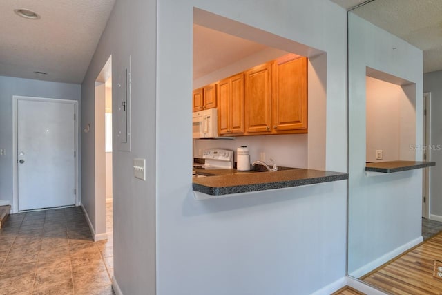 kitchen with a textured ceiling, kitchen peninsula, light tile flooring, and range