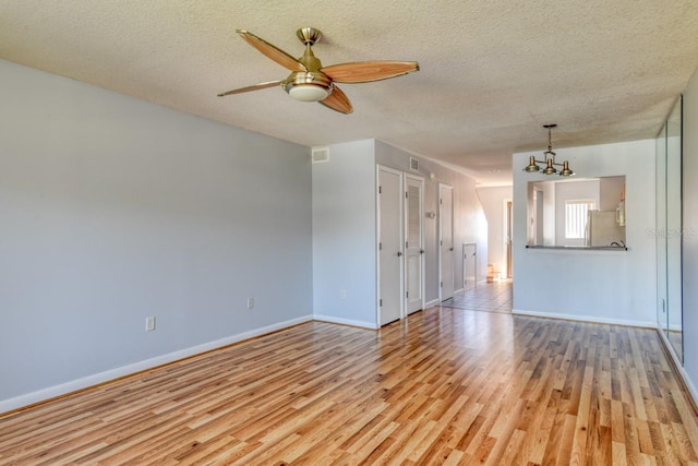 unfurnished room with ceiling fan with notable chandelier, a textured ceiling, and light wood-type flooring