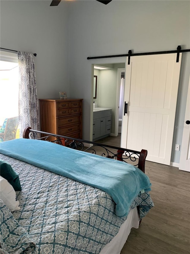 bedroom with ensuite bath, ceiling fan, a barn door, and dark wood-type flooring