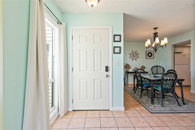 foyer with light tile flooring, a healthy amount of sunlight, a notable chandelier, and a textured ceiling