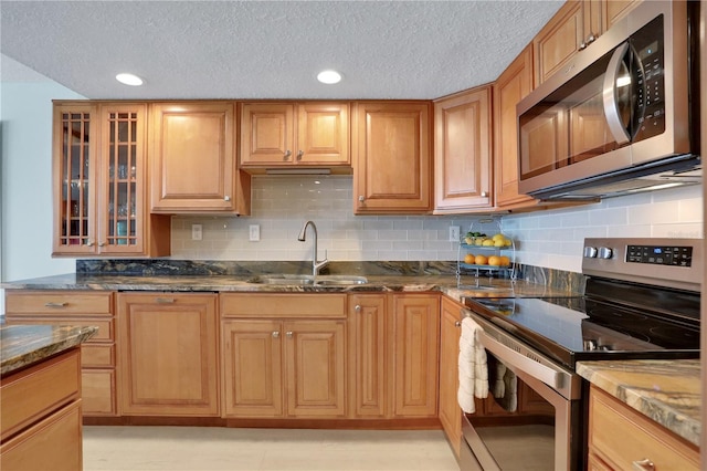 kitchen with backsplash, sink, stainless steel appliances, and dark stone counters