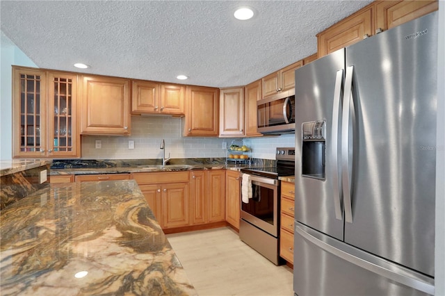 kitchen with appliances with stainless steel finishes, backsplash, dark stone counters, and light wood-type flooring