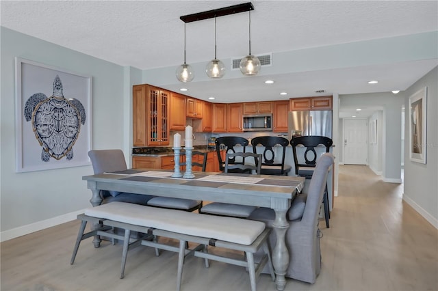 kitchen featuring appliances with stainless steel finishes, a textured ceiling, light hardwood / wood-style floors, and hanging light fixtures