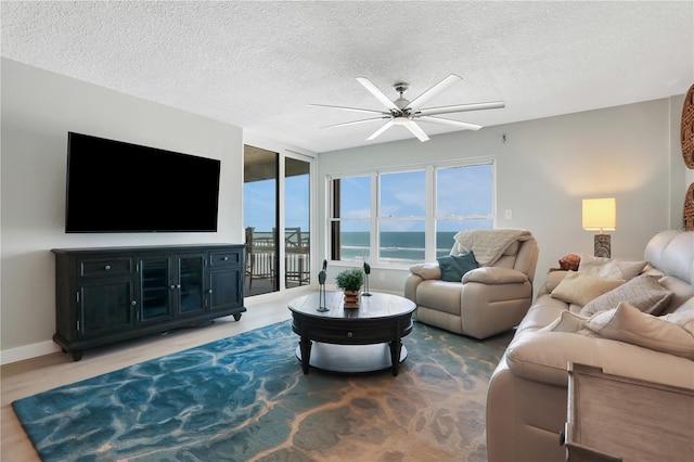 living room featuring ceiling fan, a water view, and a textured ceiling