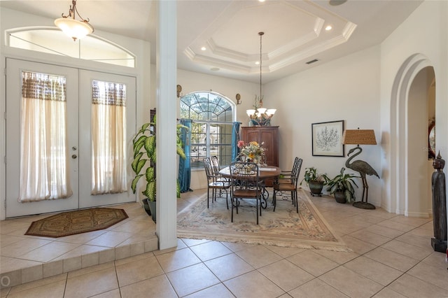 tiled entryway featuring french doors, a raised ceiling, and a chandelier