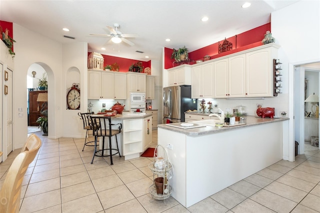 kitchen with stainless steel fridge with ice dispenser, a kitchen bar, ceiling fan, light tile flooring, and white microwave