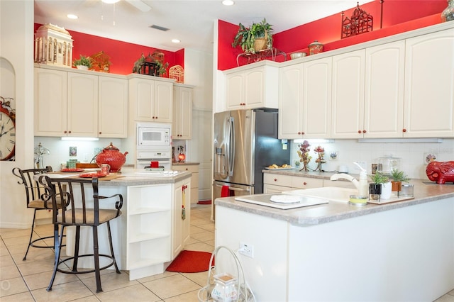 kitchen with light tile floors, a kitchen bar, white appliances, tasteful backsplash, and white cabinetry