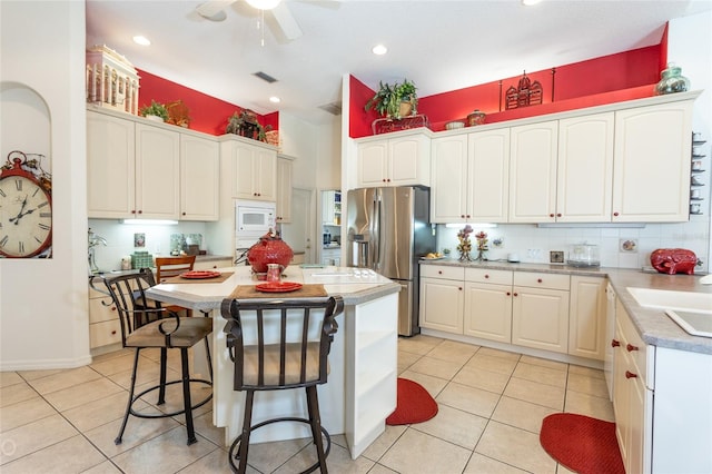 kitchen with a center island, white microwave, stainless steel fridge, and light tile flooring