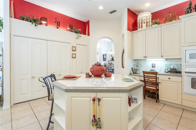 kitchen with white appliances, a center island, backsplash, and light tile floors