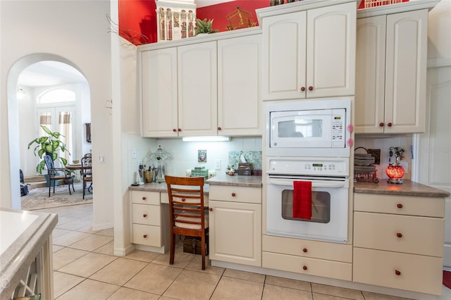 kitchen featuring backsplash, white cabinets, white appliances, and light tile floors