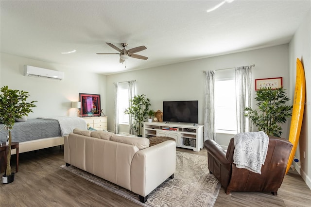 living room featuring an AC wall unit, wood-type flooring, and ceiling fan