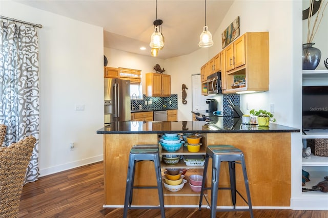 kitchen featuring kitchen peninsula, decorative light fixtures, appliances with stainless steel finishes, backsplash, and dark wood-type flooring