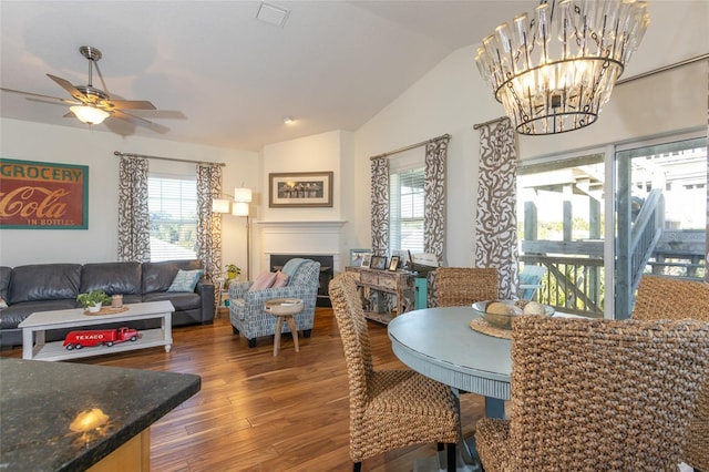 dining space with dark hardwood / wood-style flooring, a healthy amount of sunlight, ceiling fan with notable chandelier, and vaulted ceiling