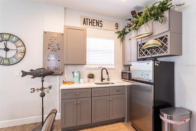 kitchen featuring stainless steel refrigerator, light hardwood / wood-style flooring, gray cabinets, and sink