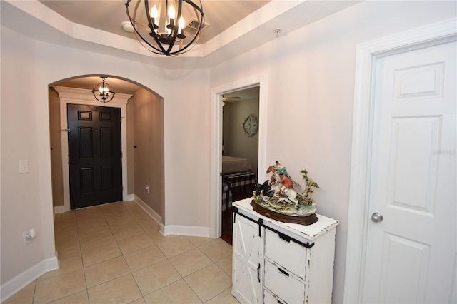 foyer entrance featuring a raised ceiling, a notable chandelier, and light tile flooring