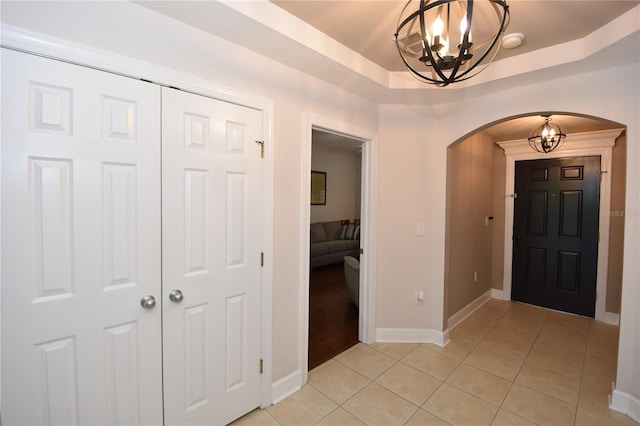 entrance foyer featuring light tile flooring, a raised ceiling, and an inviting chandelier