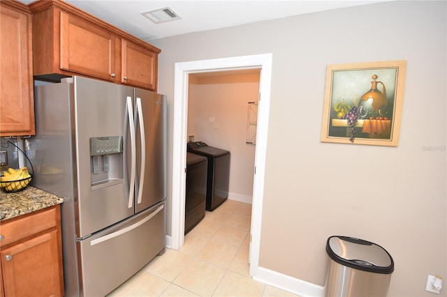 kitchen with washing machine and clothes dryer, light stone countertops, light tile flooring, and stainless steel fridge