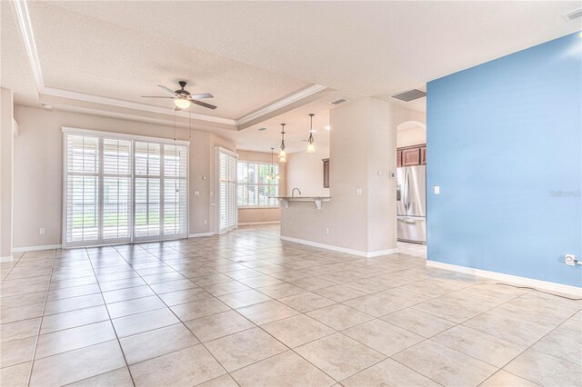 unfurnished living room with a raised ceiling, ceiling fan, plenty of natural light, and a textured ceiling