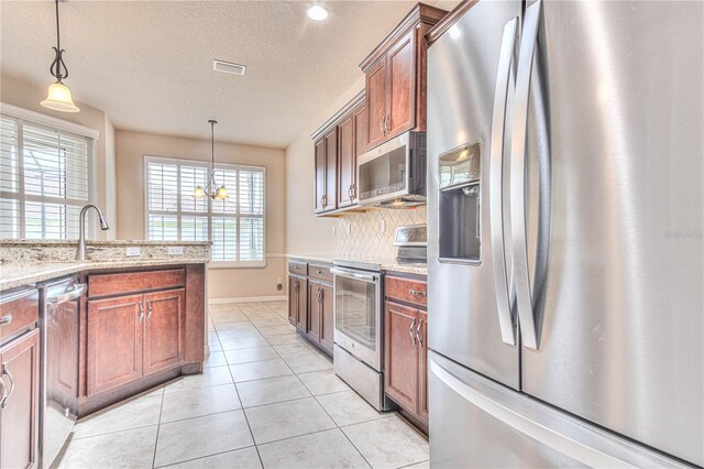 kitchen featuring hanging light fixtures, a textured ceiling, a notable chandelier, light stone counters, and stainless steel appliances