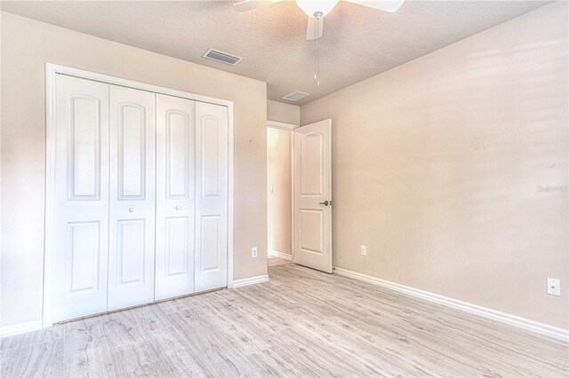 unfurnished bedroom featuring a textured ceiling, a closet, light hardwood / wood-style floors, and ceiling fan