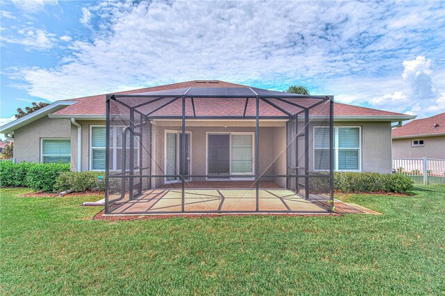 rear view of house featuring a lawn, glass enclosure, and a patio