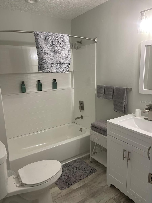 full bathroom featuring toilet, vanity with extensive cabinet space, a textured ceiling, hardwood / wood-style flooring, and bathing tub / shower combination