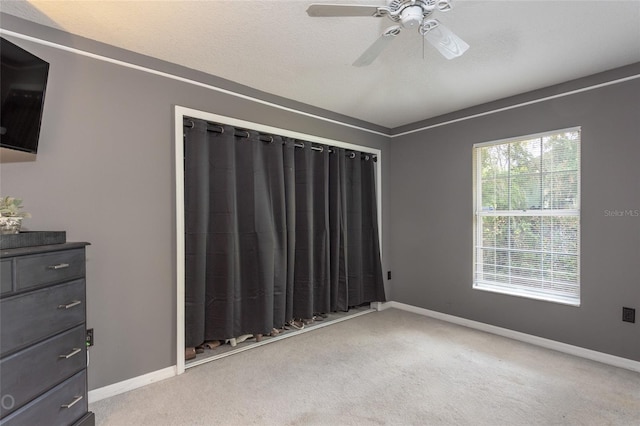 unfurnished bedroom with ceiling fan, light carpet, and a textured ceiling