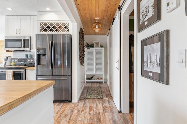 kitchen with a barn door, white cabinets, stainless steel appliances, wooden ceiling, and light hardwood / wood-style flooring