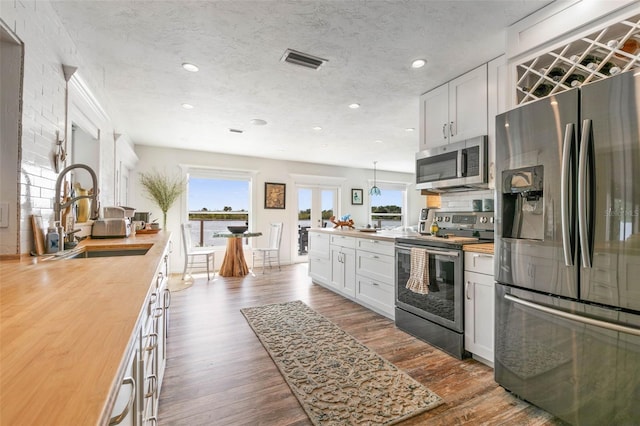 kitchen featuring white cabinets, dark wood-type flooring, stainless steel appliances, wooden counters, and a textured ceiling