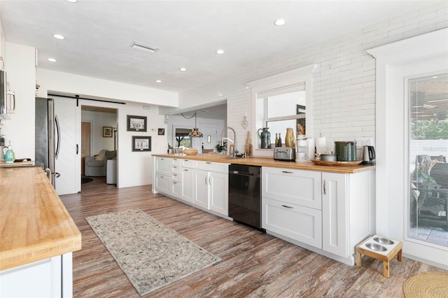 kitchen with a barn door, butcher block countertops, white cabinets, dishwasher, and stainless steel refrigerator