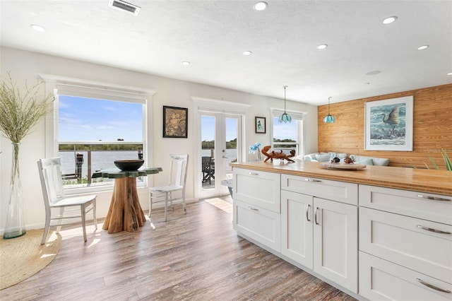 kitchen featuring white cabinets, light hardwood / wood-style floors, wooden walls, french doors, and pendant lighting