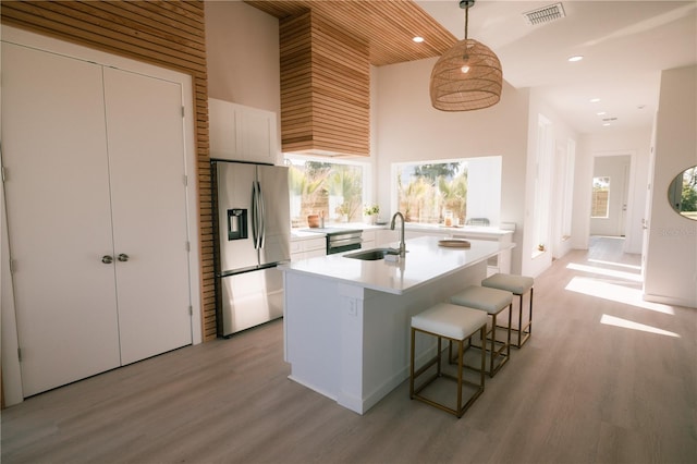 kitchen with sink, stainless steel refrigerator with ice dispenser, hanging light fixtures, a towering ceiling, and white cabinetry