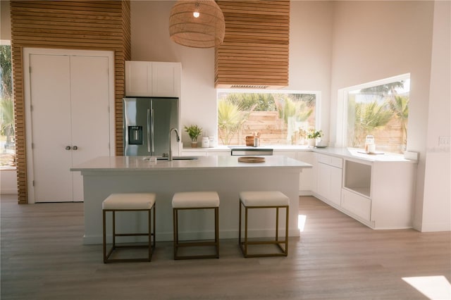 kitchen with white cabinetry, a center island, a towering ceiling, and stainless steel refrigerator with ice dispenser