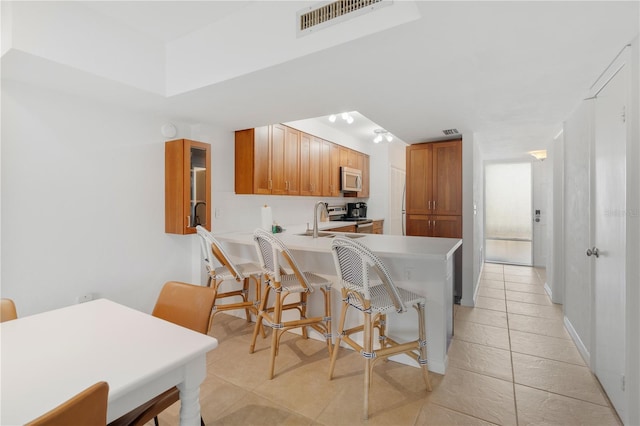 kitchen featuring kitchen peninsula, light tile patterned flooring, a breakfast bar area, and stainless steel appliances