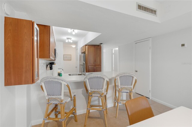 kitchen with sink, stainless steel fridge, light tile patterned floors, tasteful backsplash, and kitchen peninsula